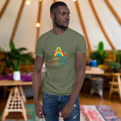 Man wearing a khaki green 100% cotton vibrant, rainbow live life in colour t-shirt in a bohemian yurt interior decorated with fairy lights, rugs, candles and plants.