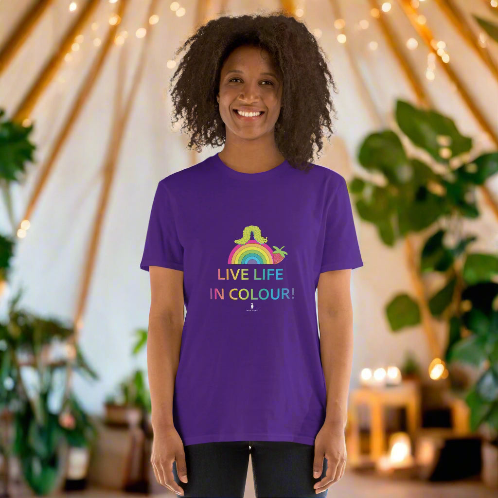 Woman wearing a purple 100% cotton vibrant, rainbow live life in colour t-shirt in a bohemian yurt interior decorated with fairy lights, rugs, candles and plants.