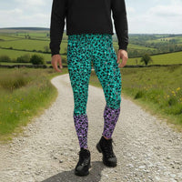 Man from the waist down wearing mens Purple and Green Leopard Glamour funky festival yoga leggings standing facing forwards with his hands by his sides. The man is standing in a park in spring with blossoming trees and pink and yellow tulips flowering. This design features an animal print pattern in black, grey and white, printed at a medium scale. The top 3/4 background is mint green with the bottom 1/4 purple