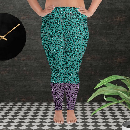A curvy woman from the waist down wearing plus-size high-waist Purple and Green Leopard Glamour funky festival yoga leggings standing facing forwards. The woman is standing in front of a textured grey background with a black and gold wall clock to the left and a partially visible leafy plant on the floor in the bottom right.  This design features an animal print pattern in black, grey and white, printed at a medium scale. The top 3/4 background is mint green with the bottom 1/4 purple