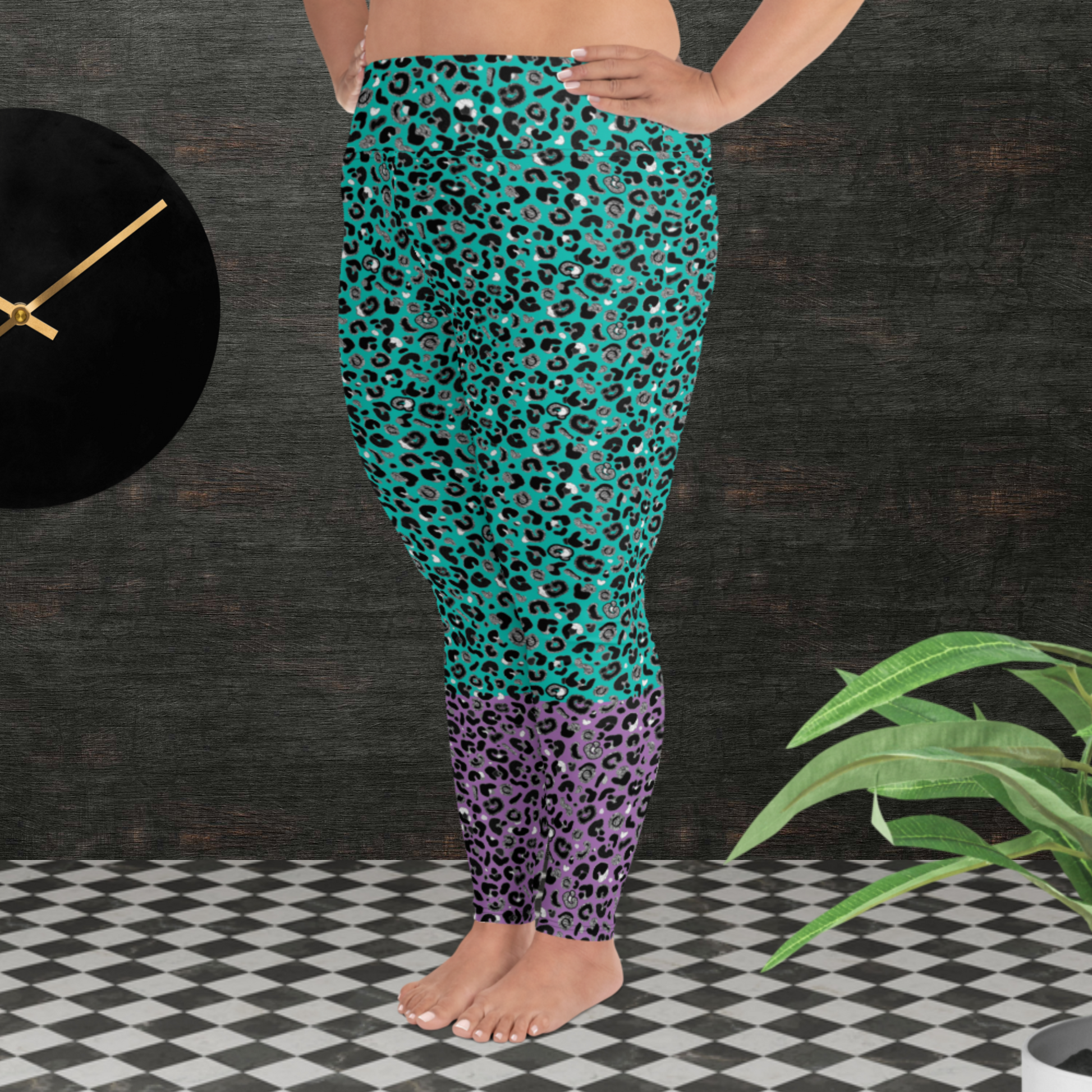 A curvy woman from the waist down wearing plus-size high-waist Purple and Green Leopard Glamour funky festival yoga leggings standing facing to the left. The woman is standing in front of a textured grey background with a black and gold wall clock to the left and a partially visible leafy plant on the floor in the bottom right.  This design features an animal print pattern in black, grey and white, printed at a medium scale. The top 3/4 background is mint green with the bottom 1/4 purple
