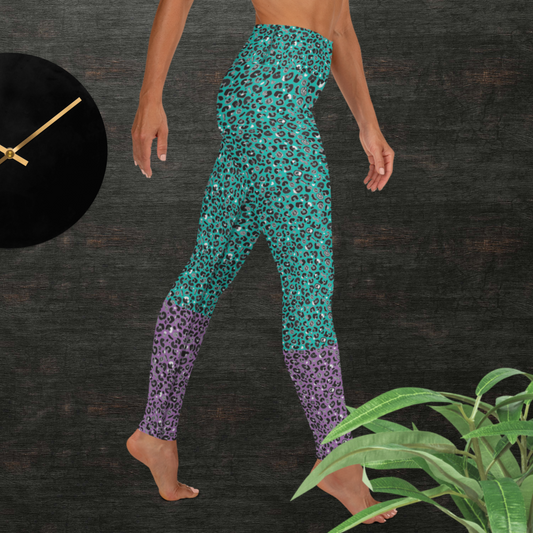 Woman from the waist down wearing high-waist Purple and Green Leopard Glamour funky festival yoga leggings standing facing to the right with her hands by her sides. The woman is standing in front of a textured grey background with a black and gold wall clock to the left and a partially visible leafy plant on the floor in the bottom right.  This design features an animal print pattern in black, grey and white, printed at a medium scale. The top 3/4 background is mint green with the bottom 1/4 purple
