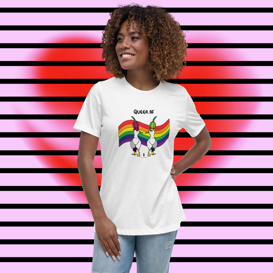 Woman standing facing forwards and looking to the left, wearing a fitted white Sassy Seagull Queer AF LGBTQ+ Pride T-Shirt and pale stonewash blue jeans. She is standing in front of a pink background with horizontal black stripes and a large, soft-focus red heart. The t-shirt is white with short sleeves. The graphic shows two cartoon style seagulls wearing colourful hats walking away in front of an LGBTQIA pride flag, underneath the wording Queer AF. It is a bold playful design for everyday wear.