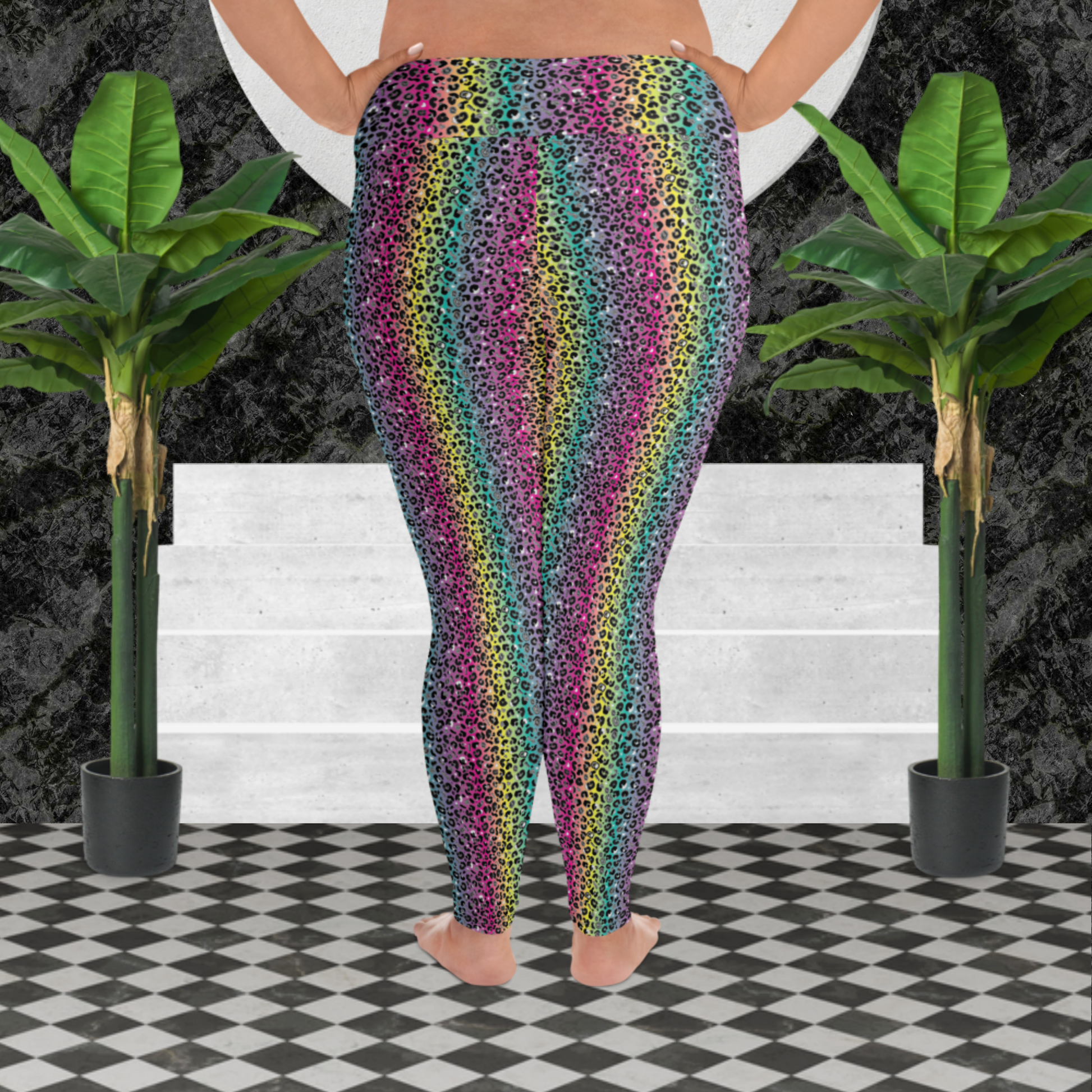 A curvy woman from the waist down wearing plus-size high-waist Rainbow Leopard Glamour funky festival yoga leggings standing facing to the back with her hands on her hips. The woman is standing on a black and white tiled floor in front of some white steps and a black and grey marble background. There is a leafy plant on the floor at each side of the steps. The rainbow leopard glamour design is an animal print pattern in black, grey and white, printed at a small scale against a blended rainbow background