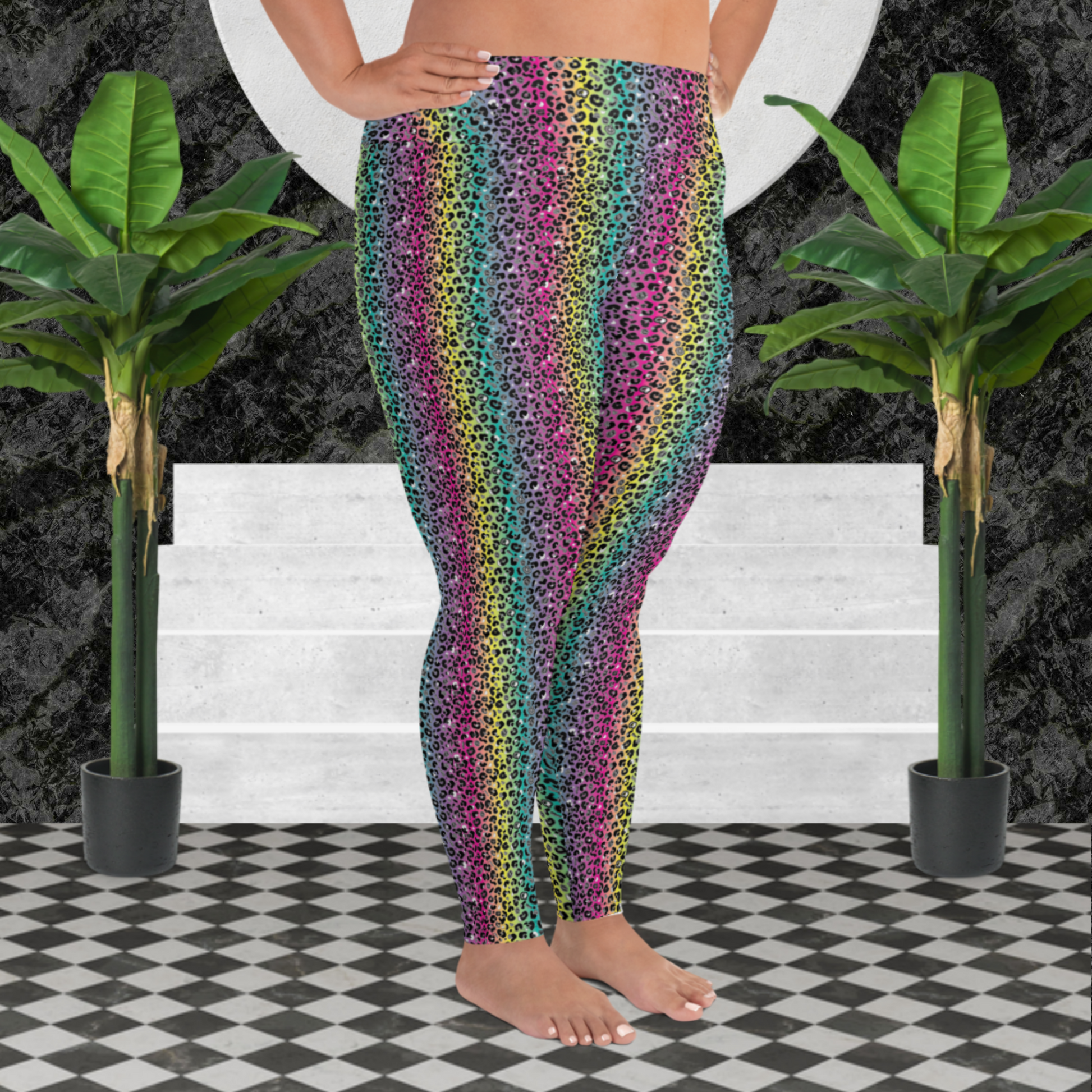 A curvy woman from the waist down wearing plus-size high-waist Rainbow Leopard Glamour funky festival yoga leggings standing facing to the right with her hands on her hips. The woman is standing on a black and white tiled floor in front of some white steps and a black and grey marble background. There is a leafy plant on the floor at each side of the steps. The rainbow leopard glamour design is an animal print pattern in black, grey and white, printed at a small scale against a blended rainbow background