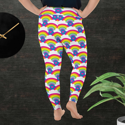 A curvy woman from the waist down wearing plus-size high-waist Rainbow Love funky festival yoga leggings standing facing backwards with both of her hands on her hips. The woman is standing in front of a textured grey background with a black and gold wall clock to the left and a partially visible leafy plant on the floor in the bottom right. The rainbow love pattern features repeating rainbows and white fluffy clouds with a small pink heart beneath each rainbow. The background colour is royal sky blue