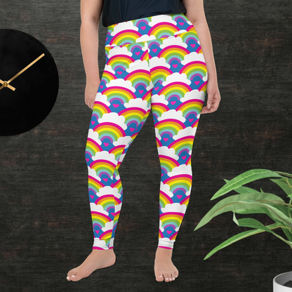 A curvy woman from the waist down wearing plus-size high-waist Rainbow Love funky festival yoga leggings standing facing forwards with her hands by her sides. The woman is standing in front of a textured grey background with a black and gold wall clock to the left and a partially visible leafy plant on the floor in the bottom right. The rainbow love pattern features repeating rainbows and white fluffy clouds with a small pink heart beneath each rainbow. The background colour is royal sky blue