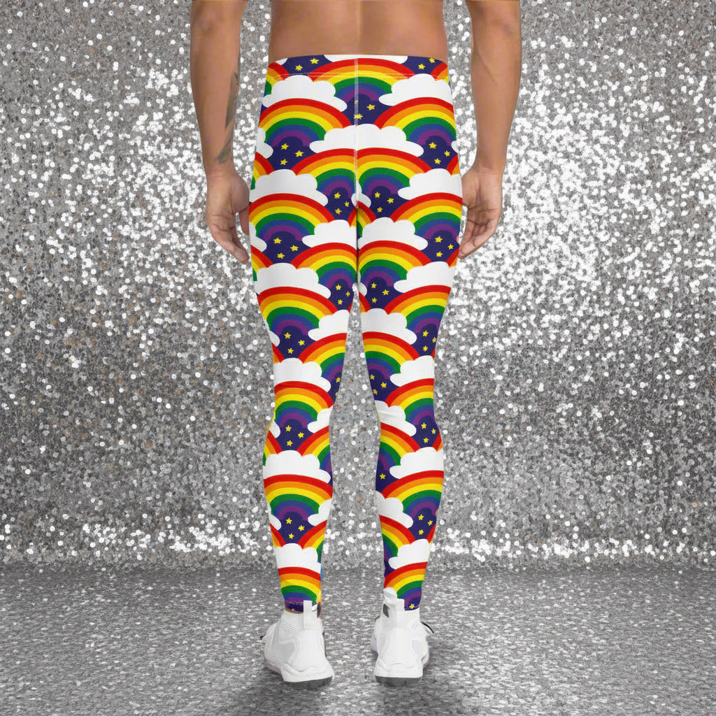 Man from the waist down wearing men's Rainbow Sparkle funky festival yoga leggings standing facing away with his hands by his sides. The man is standing in a nightclub with a colourful pink lighting glow and other club goers in the background. The rainbow sparkle pattern features repeating rainbows and white fluffy clouds with three small yellow stars beneath each rainbow. The background colour is navy blue