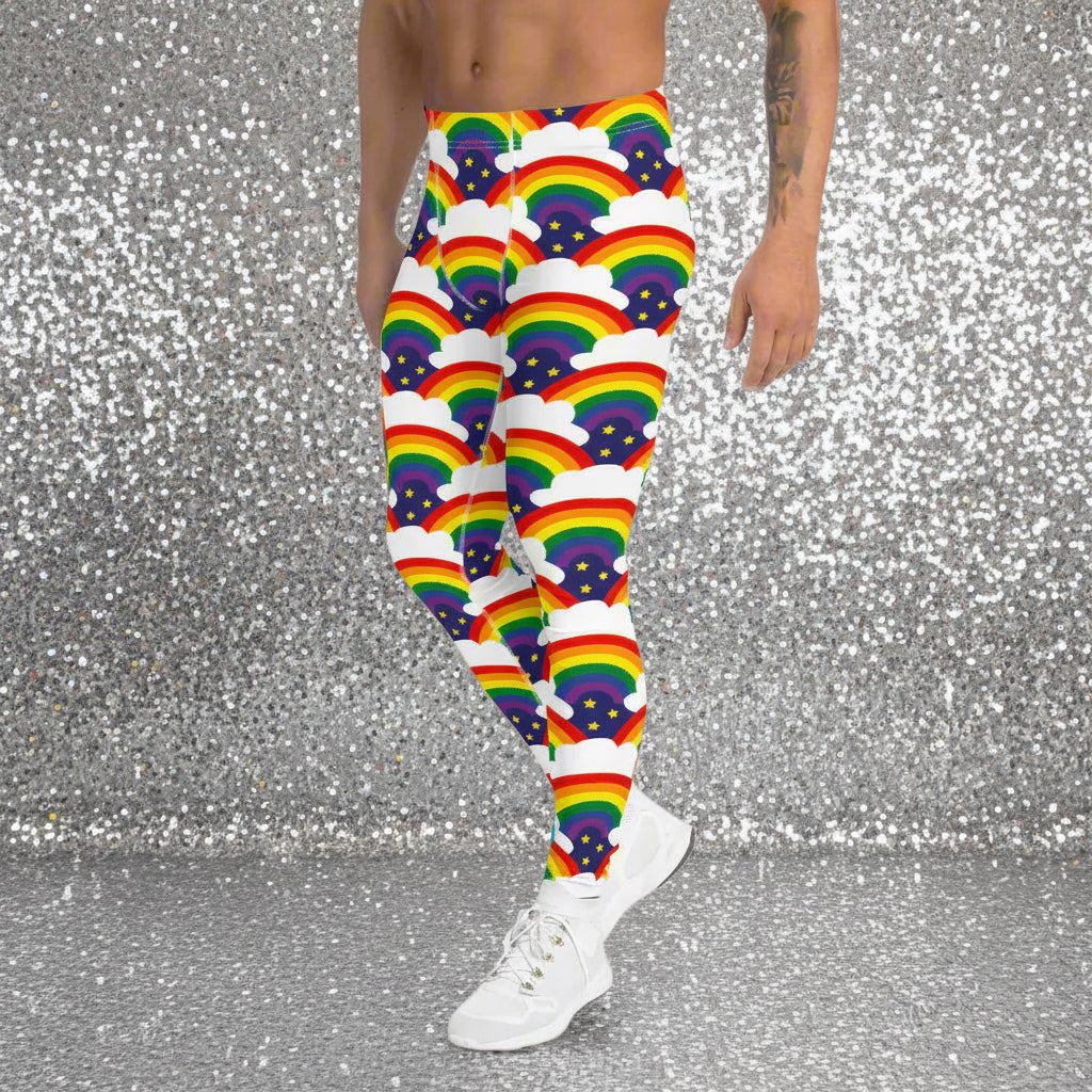 Man from the waist down wearing men's Rainbow Sparkle funky festival yoga leggings standing facing to the left with his hands by his sides. The man is standing in a nightclub with colourful pink lighting and other club goers in the background. The rainbow sparkle pattern features repeating rainbows and white fluffy clouds with three small yellow stars beneath each rainbow. The background colour is navy blue