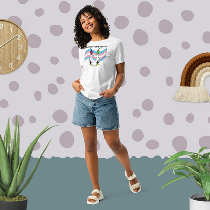 Woman posing casually facing forwards, wearing a fitted white Sassy Seagull Support Trans Youth LGBTQ+ Pride T-Shirt and  stonewash blue jean shorts. She is standing in a pastel coloured boho style room with plants either side and spotty wallpaper. The t-shirt is white with short sleeves. The graphic shows two cartoon style seagulls wearing colourful hats walking away in front of a trans pride flag, underneath the wording Support Trans Youth. It is a soft playful design for everyday wear.