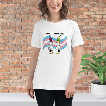 Woman standing facing forwards wearing a fitted white Sassy Seagull Proud Trans Ally LGBTQ+ Pride T-Shirt and black trousers. She is standing in front of a brick wall with a plant on a white step behind her. The t-shirt is white with short sleeves. The graphic shows two cartoon style seagulls wearing colourful hats walking away in front of an trans pride flag, underneath the wording Proud Trans Ally. It is a soft playful design for everyday wear.