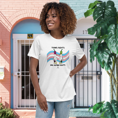 Woman standing facing forwards and looking to the left, wearing a fitted white Sassy Seagull Trans Rights are Human Rights LGBTQ+ Pride T-Shirt and pale stonewash blue jeans. She is standing in front of pink and blue houses with white doors. The t-shirt is white with short sleeves. The graphic shows two cartoon style seagulls wearing colourful hats walking away in front of a trans pride flag. The words Trans Rights sit above the image and below the words: Are Human Rights.