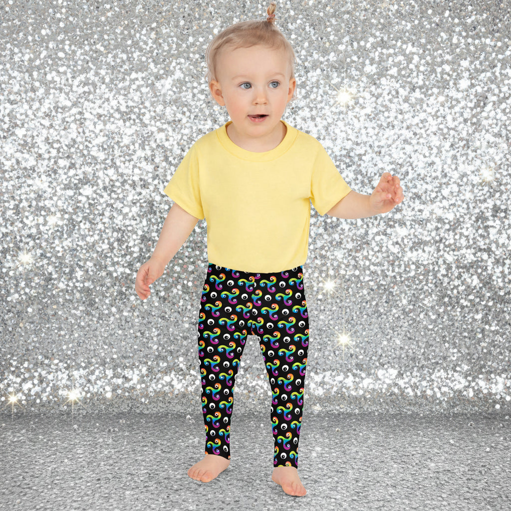 Toddler standing facing to the front wearing a pale yellow t-shirt and trippy triskelion leggings in a natural field background.