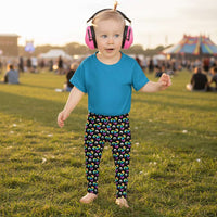 Toddler standing facing to the front wearing a pale yellow t-shirt and trippy triskelion leggings in a natural field background.