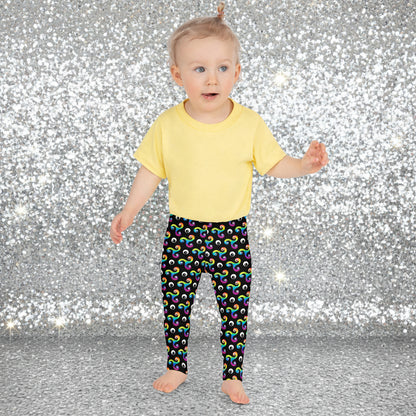 Toddler standing facing to the front wearing a pale yellow t-shirt and trippy triskelion leggings in a natural field background.