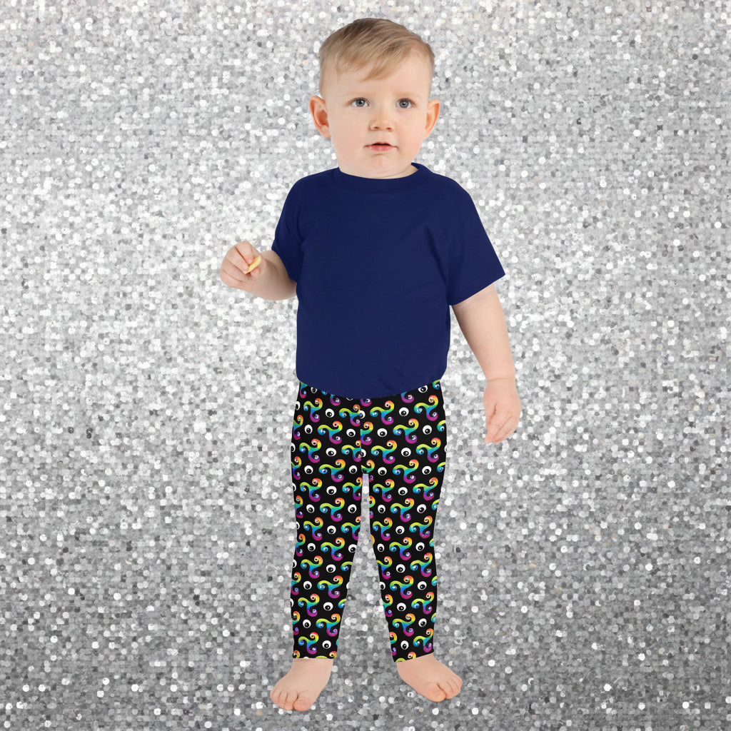 Toddler standing facing  forward wearing a blue t-shirt and trippy triskelion leggings in a soft play centre.