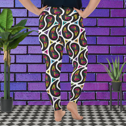 A curvy woman from the waist down wearing plus-size white Paisley Party high-waist funky festival yoga leggings standing facing to the back with her hands on her hips. The woman is standing on a black and white tiled floor in front of a vivid purple brick wall with 2 leafy green plants on the floor, one on either side.The Paisley Party pattern is a repeating paisley pattern. The paisley shapes are filled with decorative detail in a variety of bright colours against a white background.