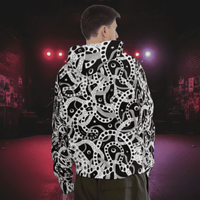 Man from the chin down to the waist, posing standing facing away wearing a 100% cotton bold black and white Who's Afraid Of The Dark all-over print hoodie. He is standing in a park with trees in the background. The hoodie has an abstract design made up of interwoven shapes detailed with spots, stars and lines. It is a unique and bold design for everyday wear.