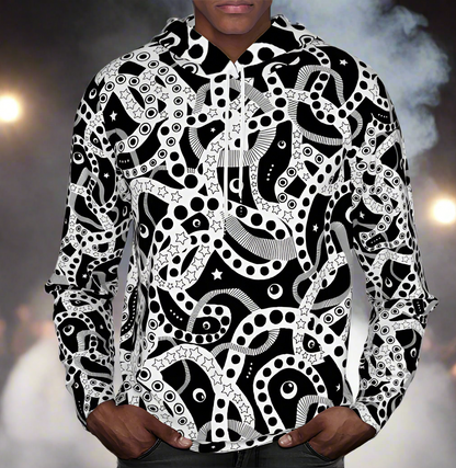 Man from the chin down to the waist, posing standing facing forwards wearing a 100% cotton bold black and white Who's Afraid Of The Dark all-over print hoodie. He is standing against a stage background with lights and smoke effects. The hoodie has an abstract design made up of interwoven shapes detailed with spots, stars and lines. It is a unique and bold design for everyday wear.