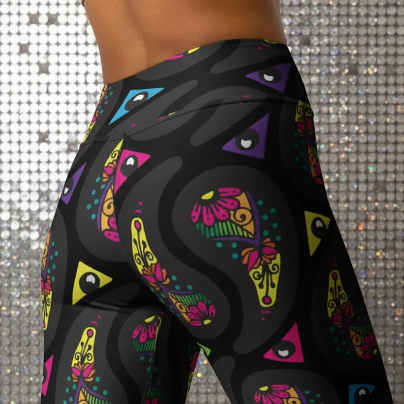 High waist Black Paisley Party festival yoga leggings close up back view. Woman is standing in a boho interior room.  The Paisley Party design is a bold colourful rainbow geometric print pattern. Designed in Wales, UK | Sassy Seagull. 