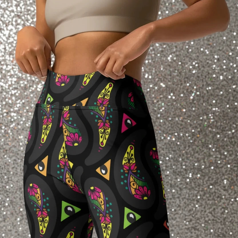 High waist Black Paisley Party festival yoga leggings close up front view. Woman is standing in a boho interior room.  The Paisley Party design is a bold colourful rainbow geometric print pattern. Designed in Wales, UK | Sassy Seagull. 