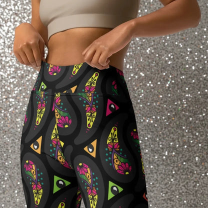 High waist Black Paisley Party festival yoga leggings close up front view. Woman is standing in a boho interior room.  The Paisley Party design is a bold colourful rainbow geometric print pattern. Designed in Wales, UK | Sassy Seagull. 