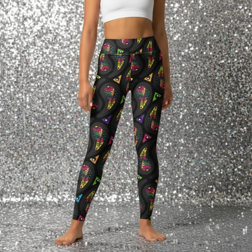 High waist Black Paisley Party festival yoga leggings front view. Woman is standing in a boho interior room.  The Paisley Party design is a bold colourful rainbow geometric print pattern. Designed in Wales, UK | Sassy Seagull. 