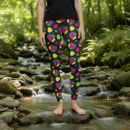 High waist Funk Party Original festival yoga leggings front view. The woman is standing in a rustic boho setting with plants, fairy lights and bunting in the background.  The Funk Party design is a bold colourful abstract print. Designed in Wales, UK | Sassy Seagull. 