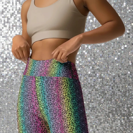 High waist Rainbow Leopard Glamour festival yoga leggings close up front view. The woman is standing in a rustic boho setting with plants, fairy lights and bunting in the background.  The rainbow leopard glamour design is a bold animal printed pattern in black, grey and white against a blended rainbow background. Designed in Wales, UK | Sassy Seagull. 