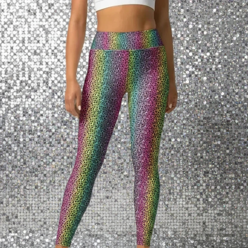 High waist Rainbow Leopard Glamour festival yoga leggings front view. The woman is standing in a rustic boho setting with plants, fairy lights and bunting in the background.  The rainbow leopard glamour design is a bold animal printed pattern in black, grey and white against a blended rainbow background. Designed in Wales, UK | Sassy Seagull.