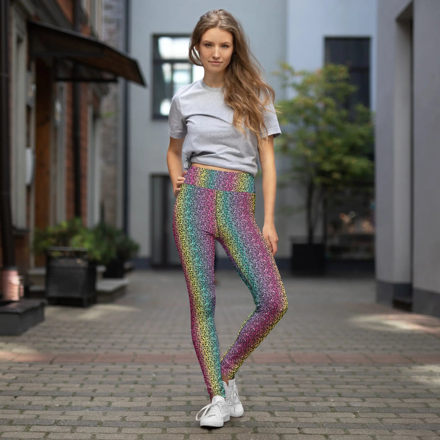 High waist Rainbow Leopard Glamour festival yoga leggings lifestyle view. The woman is standing in an outdoor setting wearing a grey t-shirt and white trainers.  The rainbow leopard glamour design is a bold animal printed pattern in black, grey and white against a blended rainbow background. Designed in Wales, UK | Sassy Seagull. 