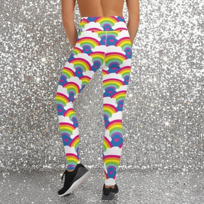 High waist Rainbow Love festival yoga leggings back view. The woman is standing in a rustic boho setting with plants, fairy lights and bunting in the background.  The Rainbow Love design is a bold design featuring rainbows, white clouds and pink hearts. Designed in Wales, UK | Sassy Seagull. 