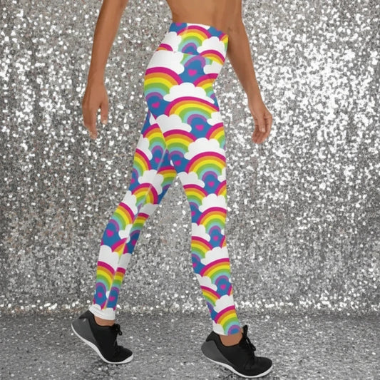 High waist Rainbow Love festival yoga leggings right view. The woman is standing in a rustic boho setting with plants, fairy lights and bunting in the background.  The Rainbow Love design is a bold design featuring rainbows, white clouds and pink hearts. Designed in Wales, UK | Sassy Seagull. 