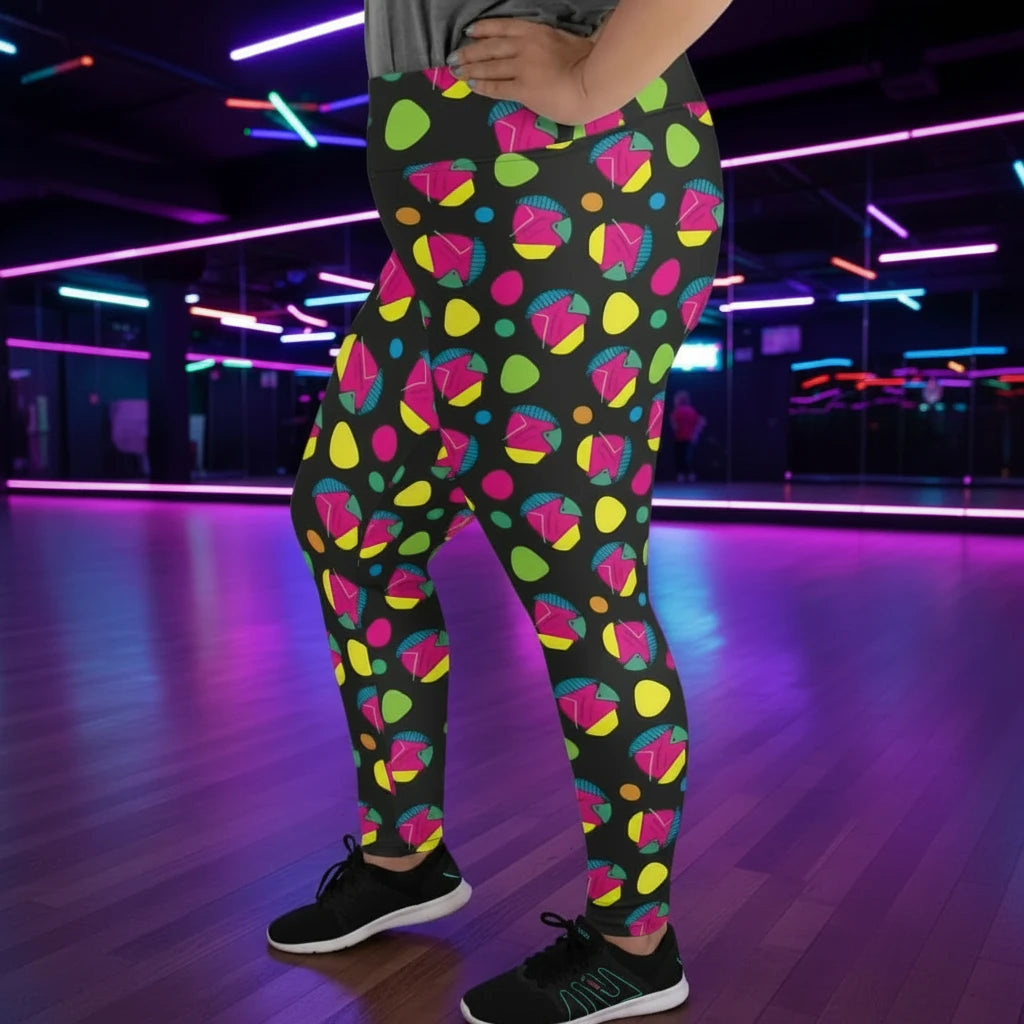 Plus-size high waist Funk Party Original festival yoga leggings side view. The woman is standing in a rustic boho setting with plants, fairy lights and bunting in the background.  The Funk Party design is a bold colourful abstract print. Designed in Wales, UK | Sassy Seagull. 