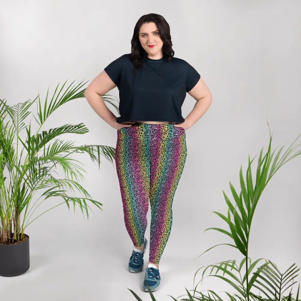 High waist Rainbow Leopard Glamour festival yoga leggings lifestyle view. The woman is standing in an indoor setting wearing a dark t-shirt and blue trainers.  The rainbow leopard glamour design is a bold animal printed pattern in black, grey and white against a blended rainbow background. Designed in Wales, UK | Sassy Seagull. 