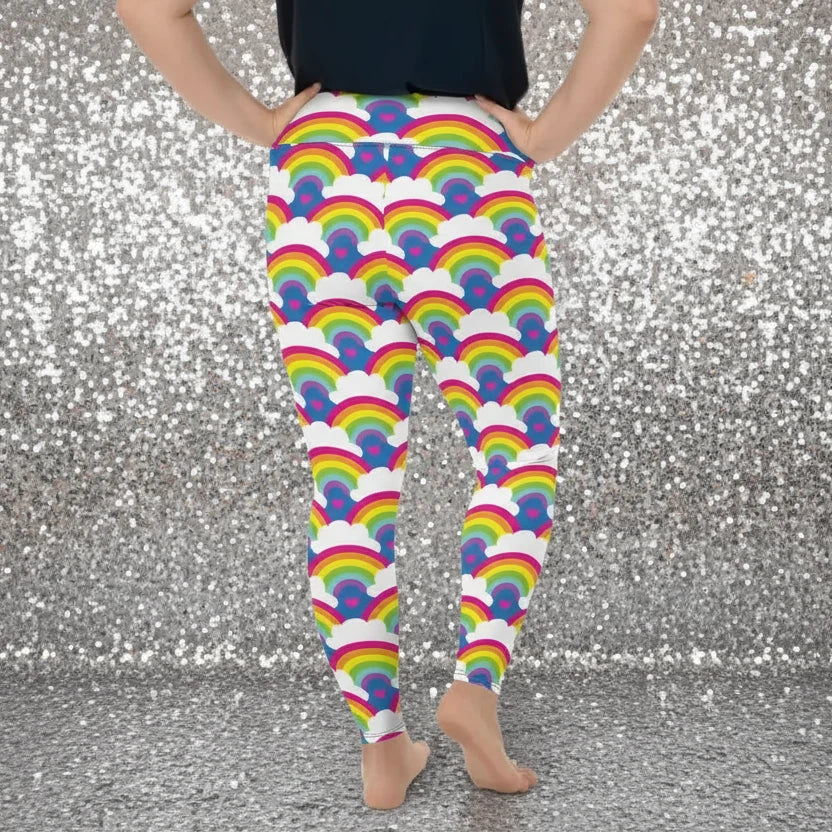 Plus-size high waist Rainbow Love festival yoga leggings back view. The woman is standing in a rustic boho setting with plants, fairy lights and bunting in the background.  The Rainbow Love design is a bold design featuring rainbows, white clouds and pink hearts. Designed in Wales, UK | Sassy Seagull. 