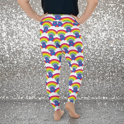 Plus-size high waist Rainbow Love festival yoga leggings back view. The woman is standing in a rustic boho setting with plants, fairy lights and bunting in the background.  The Rainbow Love design is a bold design featuring rainbows, white clouds and pink hearts. Designed in Wales, UK | Sassy Seagull. 