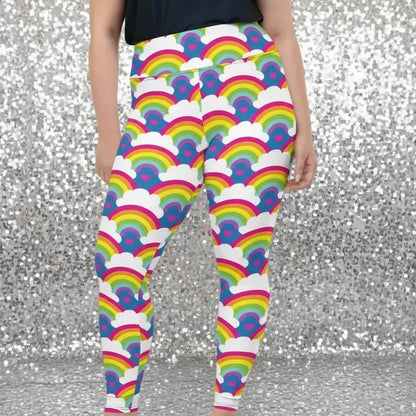 Plus-size high waist Rainbow Love festival yoga leggings front view. The woman is standing in a rustic boho setting with plants, fairy lights and bunting in the background.  The Rainbow Love design is a bold design featuring rainbows, white clouds and pink hearts. Designed in Wales, UK | Sassy Seagull. 