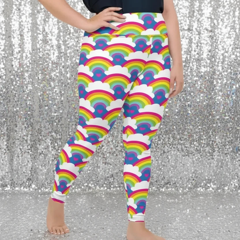 Plus-size high waist Rainbow Love festival yoga leggings right view. The woman is standing in a rustic boho setting with plants, fairy lights and bunting in the background.  The Rainbow Love design is a bold design featuring rainbows, white clouds and pink hearts. Designed in Wales, UK | Sassy Seagull. 