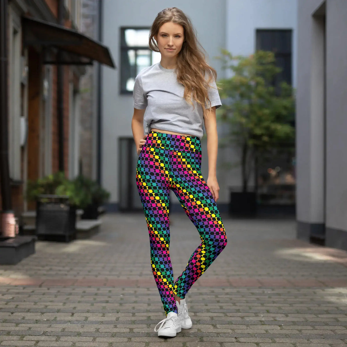 Women's high waist Rainbow Geometric yoga festival leggings lifestyle view. Woman is standing in an empty urban street. The Disco Lights design is a bold colourful rainbow spotty pattern. Designed in Wales, UK | Sassy Seagull. 