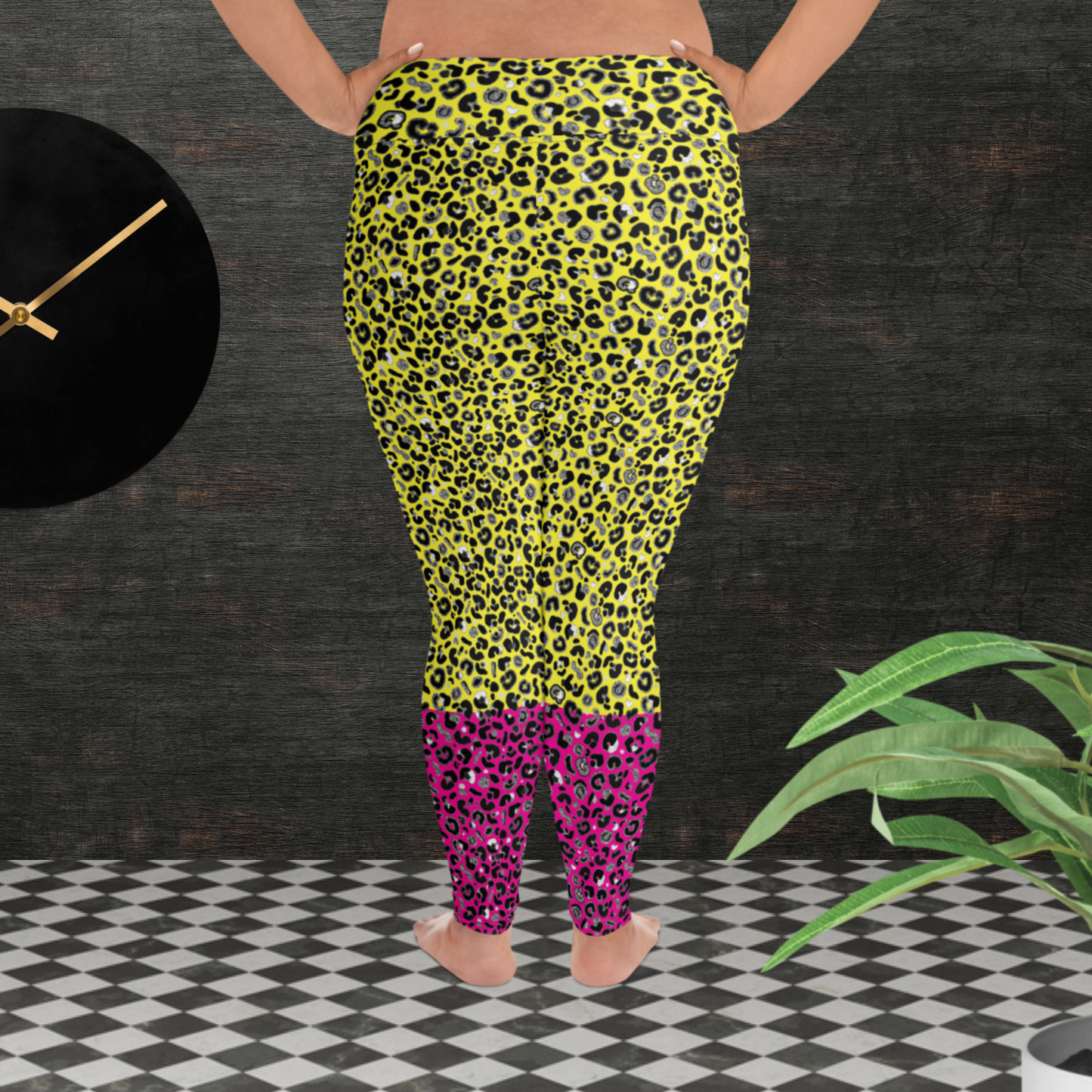 A curvy woman from the waist down wearing plus-size high-waist Yellow and Pink Leopard Glamour funky festival yoga leggings standing facing away. The woman is standing in front of a textured grey background with a black and gold wall clock to the left and a partially visible leafy plant on the floor in the bottom right.  This design features an animal print pattern in black, grey and white, printed at a medium scale. The top 3/4 background is bright yellow with the bottom 1/4 a hot pink colour