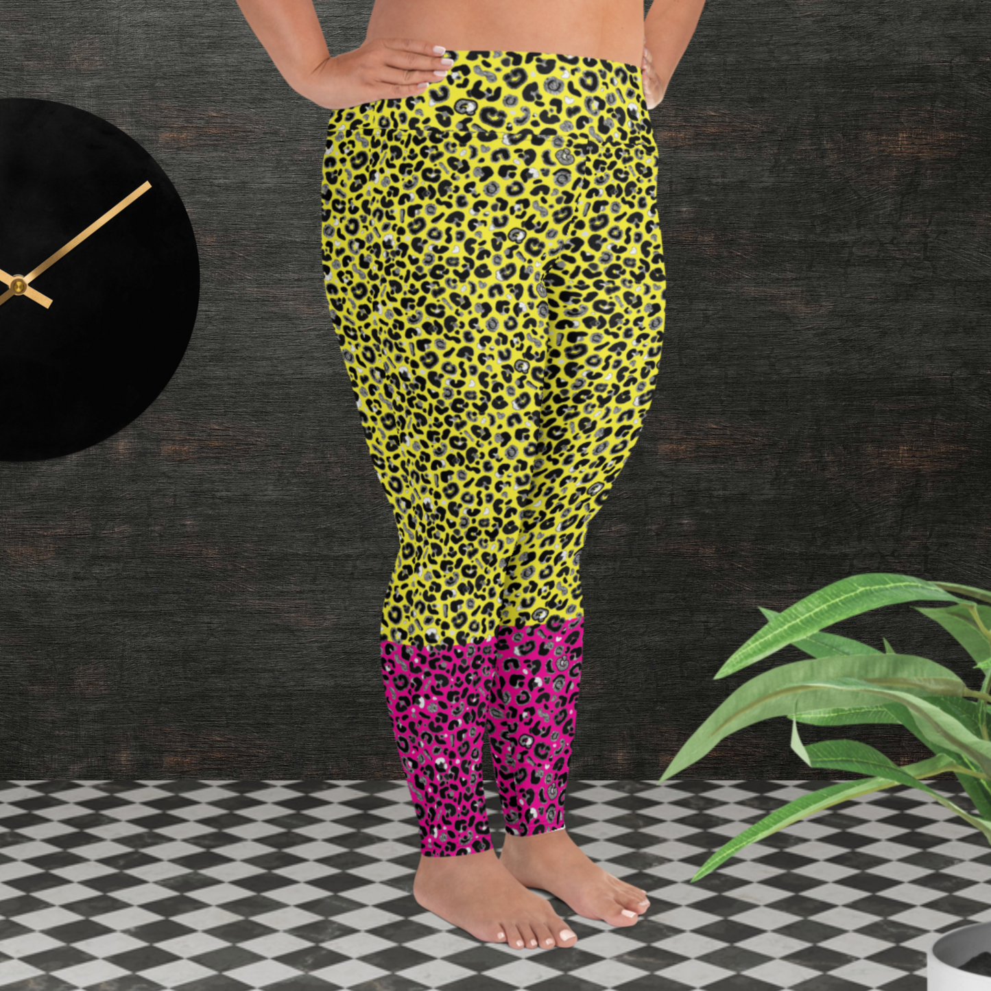 A curvy woman from the waist down wearing plus-size high-waist Yellow and Pink Leopard Glamour funky festival yoga leggings standing facing right. The woman is standing in front of a textured grey background with a black and gold wall clock to the left and a partially visible leafy plant on the floor in the bottom right.  This design features an animal print pattern in black, grey and white, printed at a medium scale. The top 3/4 background is bright yellow with the bottom 1/4 a hot pink colour