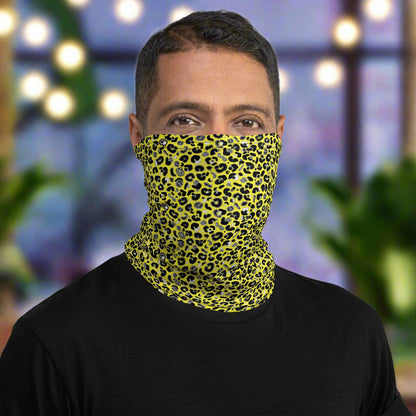 Man with short dark hair facing to the front wearing a black long sleeve top and a vibrant yellow and pink neck gaiter around his neck, covering his nose and mouth. In the background are some fairy lights and plants. This design features an animal print pattern in black, grey and white, printed at a medium scale. The top 3/4 background is bright yellow with the bottom 1/4 a hot pink colour. In this image the pink is not seen.