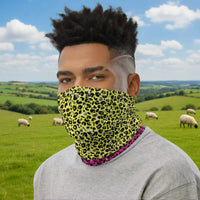 Man with short afro hair facing to the left wearing a grey long sleeve top and a vibrant yellow and pink neck gaiter around his neck, covering his nose and mouth. In the background are some fairy lights and plants. This design features an animal print pattern in black, grey and white, printed at a medium scale. The top 3/4 background is bright yellow with the bottom 1/4 a hot pink colour