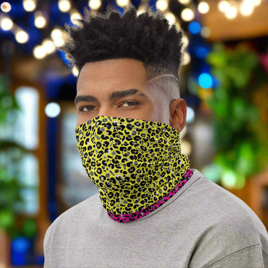 Man with short afro hair facing to the left wearing a grey long sleeve top and a vibrant yellow and pink neck gaiter around his neck, covering his nose and mouth. In the background are some fairy lights and plants. This design features an animal print pattern in black, grey and white, printed at a medium scale. The top 3/4 background is bright yellow with the bottom 1/4 a hot pink colour