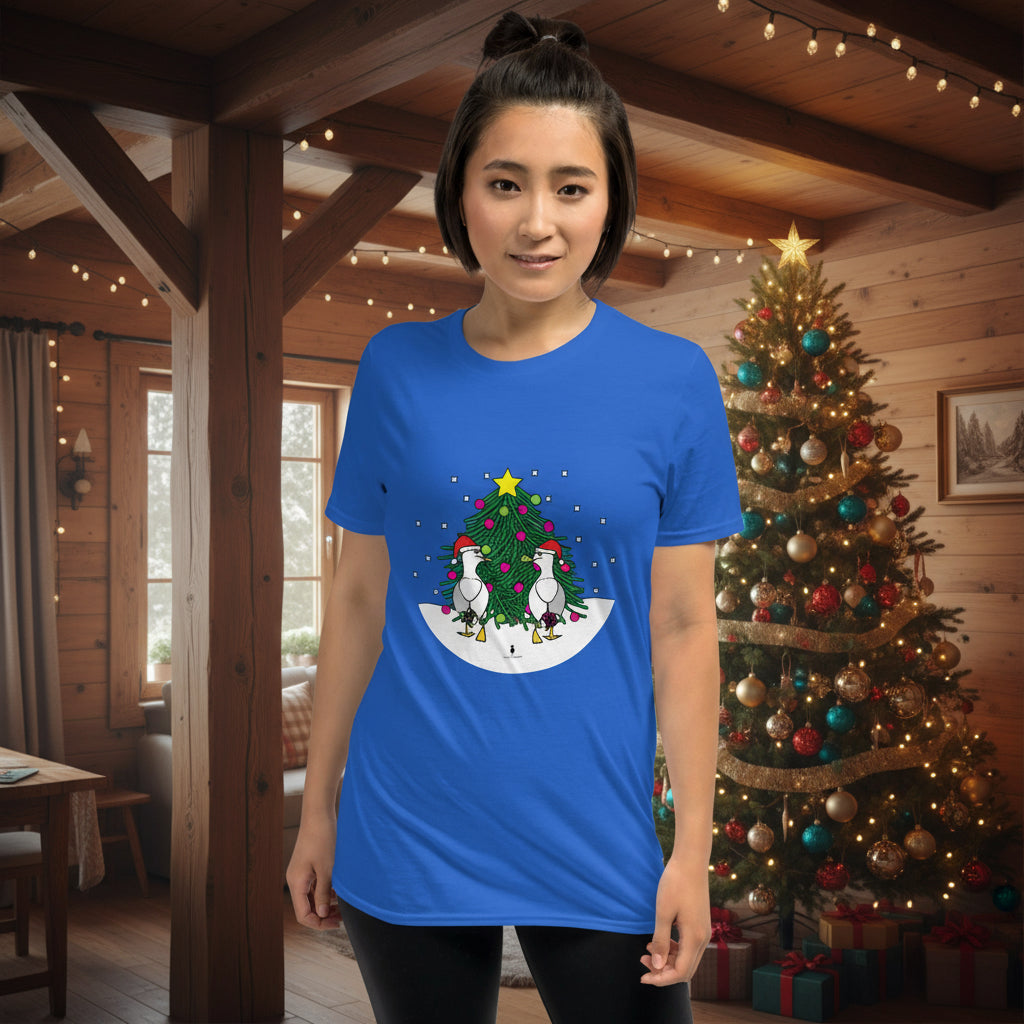 Person wearing a royal blue 100% cotton Christmas t-shirt with two sassy seagulls in front of a decorated Christmas tree. The person is standing in a wooden chalet decorated for Christmas.