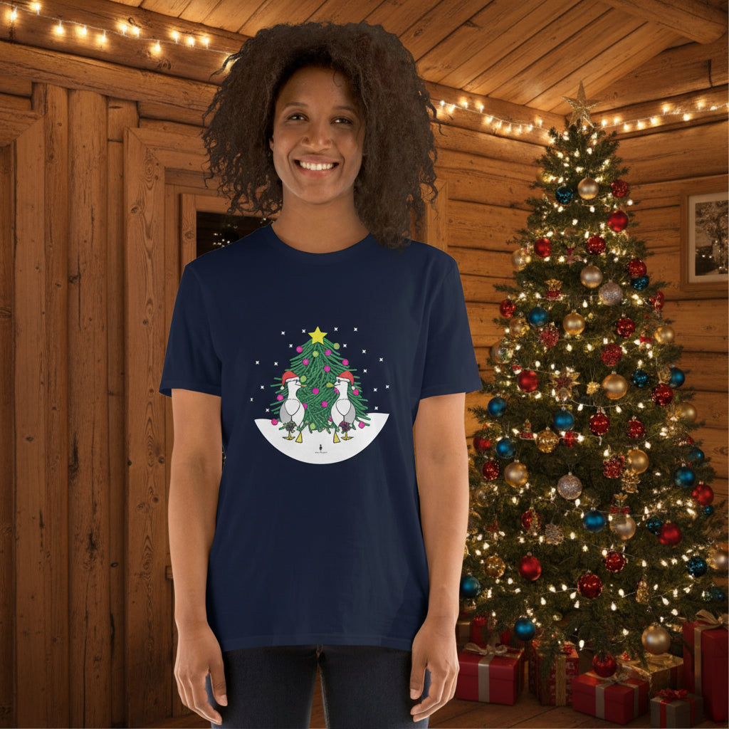 Person wearing a navy blue 100% cotton Christmas t-shirt with two sassy seagulls in front of a decorated Christmas tree. The person is standing in a wooden chalet decorated for Christmas.