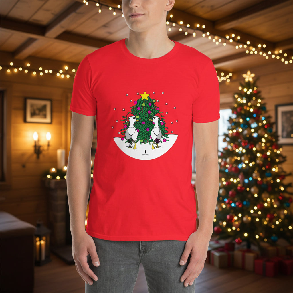 Person wearing a red 100% cotton Christmas t-shirt with two sassy seagulls in front of a decorated Christmas tree. The person is standing in a wooden chalet decorated for Christmas.