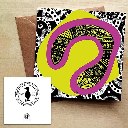 Abstract greeting card with a pop of pink and yellow and a background in black and white. The card comes with a brown envelope and is on a wooden table.