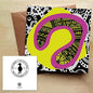 Abstract greeting card with a pop of pink and yellow and a background in black and white. The card comes with a brown envelope and is on a wooden table.